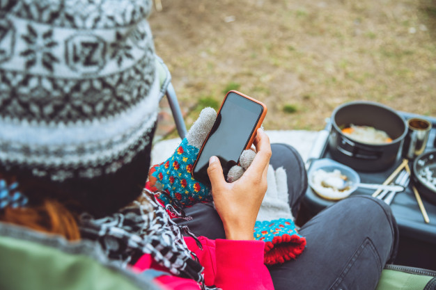 Camper relaxing with smartphone while winter camping